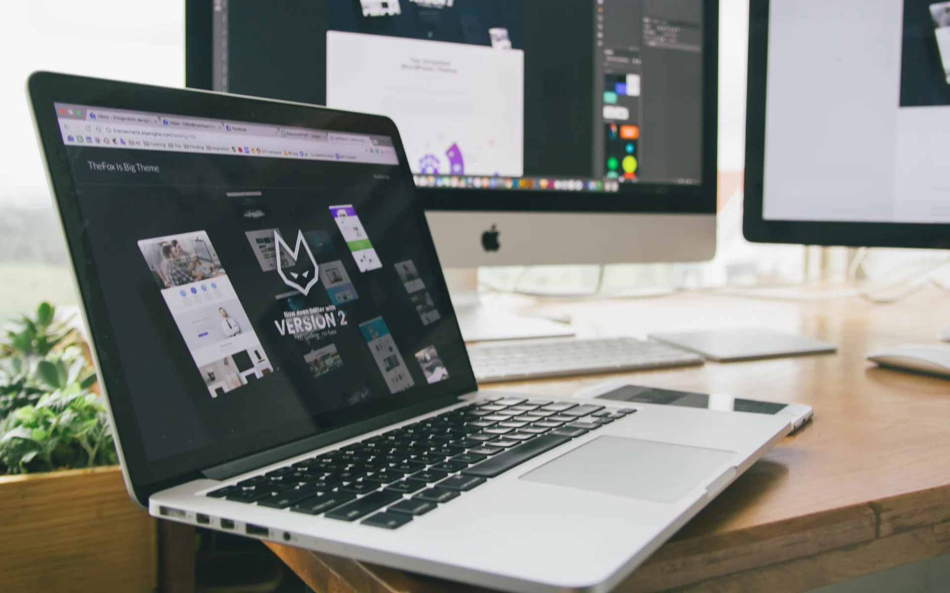 Website process on Simple Sites showing Version 2 web design with fox logo across laptop and dual monitors.